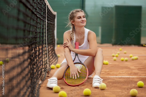 Happy smiling girl is chilling near tennis net at tennis court with racquet in hands. © volody10