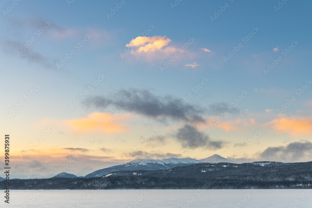 Impressive sunrise over a winter frozen lake snowy covered in northern Canada during December when the sun doesn't rise for long. Days are short, snow capped mountains, tourism, tourist, explorers. 