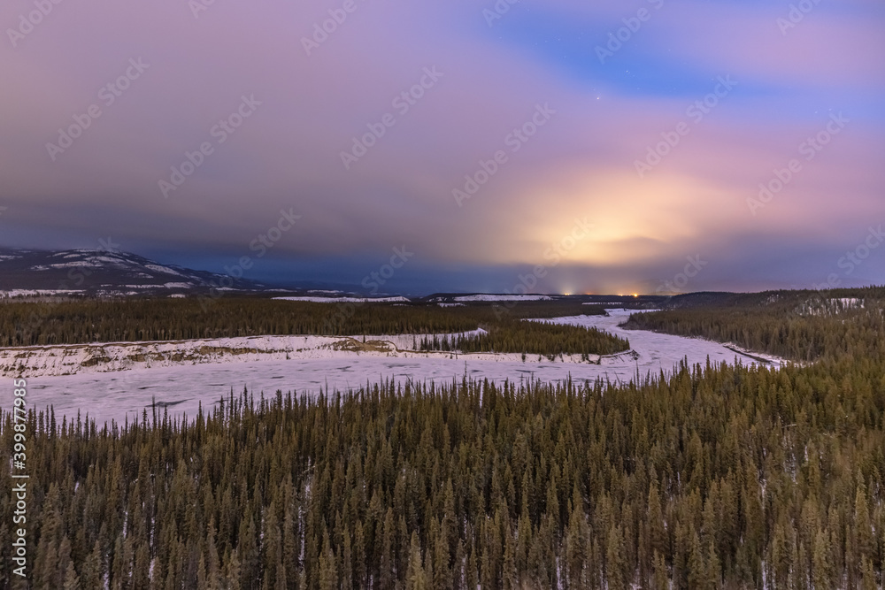 Winding Yukon River near Whitehorse, Yukon Territory at sunset in the winter time with stunning wilderness woods, forest and clouds.