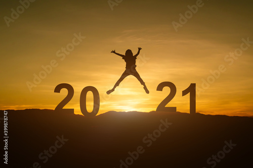 Silhouette of young woman jumping to Happy new year 2021 in sunset or sunrise background.