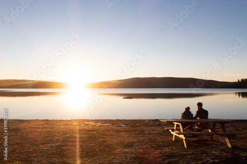 Couple sitting at a picnic table and admiring the sunset over the lake Touladi in the Temiscouata national park, Canada