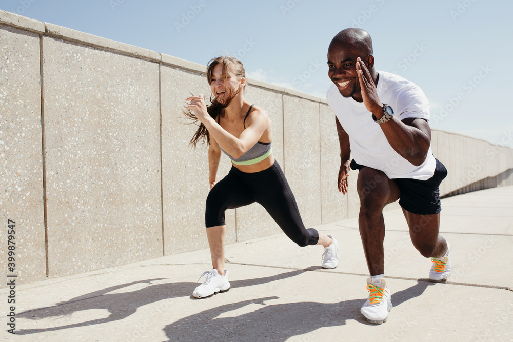 Jamaican man in white t-shirt and black shorts running with woman in grey top and black fitness leggins on fresh air and sunny weather. Jamaican man in white t-shirt and black shorts running with woman in grey top and black fitness leggins on fresh air and sunny weather.