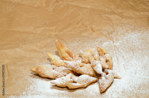 A crisp brushwood cookie, sprinkled with powdered sugar, lies on crumpled paper. Selective focus