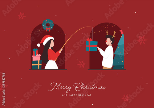 A woman in Santa hat giving a Christmas gift box to a man in reindeer headband by fishing rod. Social distancing concept. Quarantine Christmas card in a covid-19 world. Neighbors at the window.