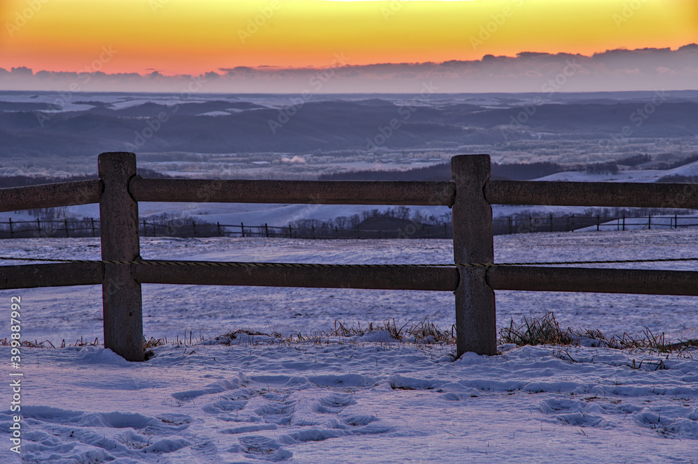Stockfoto 冬の田舎の風景 オレンジ色に染まる夜明けの空と雪原の柵 Adobe Stock