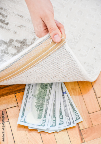 woman hidden dollar banknotes under carpet. Economy concept, saving money.
