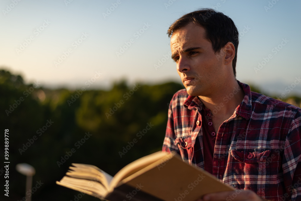 A handsome attractive young man at his home terrace reading an old book during covid quarantine confinement on a warm sunny day at the golden hour A handsome attractive young man at his home terrace reading an old book during covid quarantine confinement on a warm sunny day at the golden hour