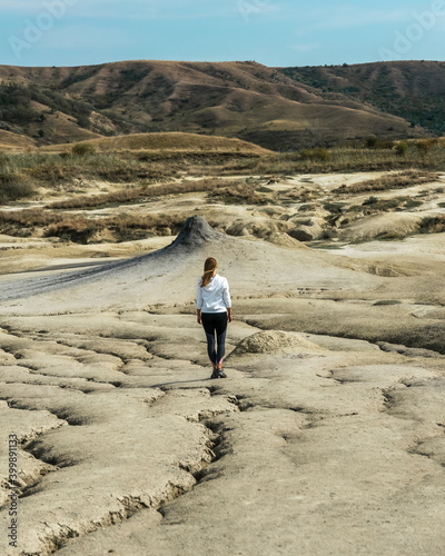 Young girl facing a mud volcano standing on cracked dry soil