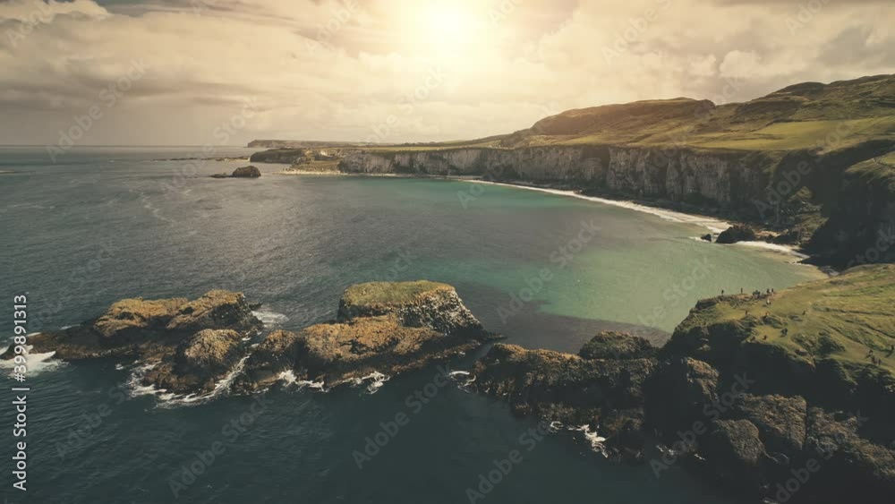 Autumn sun ocean bay aerial. Nature landscape at rock islands with tourists. People walk on isle at sea coast. Serene seascape at sunlight. Carrick Islet, Northern Ireland, United Kingdom, Europe Autumn sun ocean bay aerial. Nature landscape at rock islands with tourists. People walk on isle at sea coast. Serene seascape at sunlight. Carrick Islet, Northern Ireland, United Kingdom, Europe