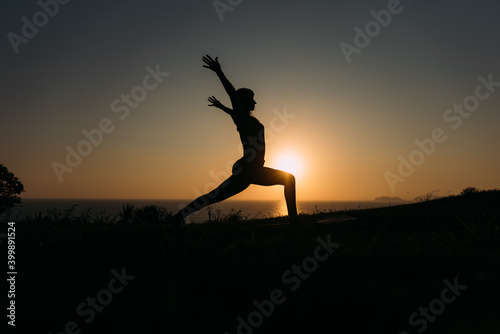 Silhouette of a slim female figure in front of the sea at sunset practicing yoga. Copy Sapce