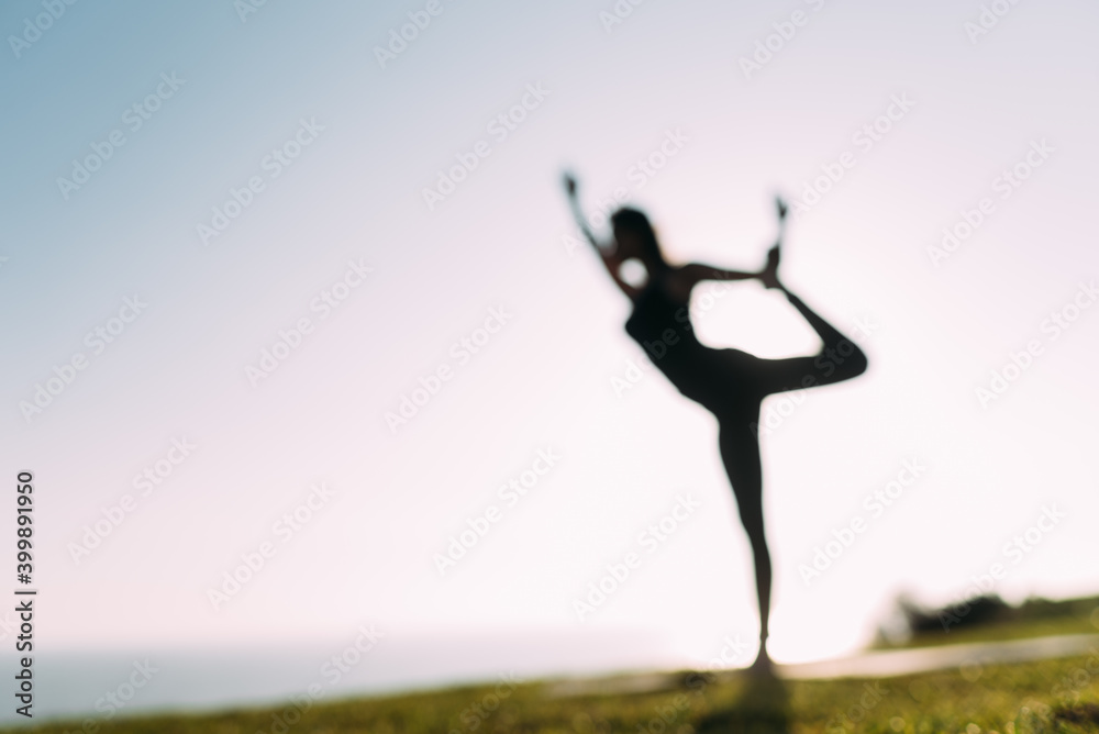 Interesting blur of a woman showing her slim figure in a Yoga position. Out of focus backlighting of a silhouette of a yogi woman. Copy space