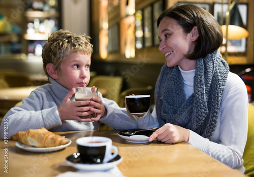 Cheerful woman spending time with her preteen son in cozy cafe. Happy family moments