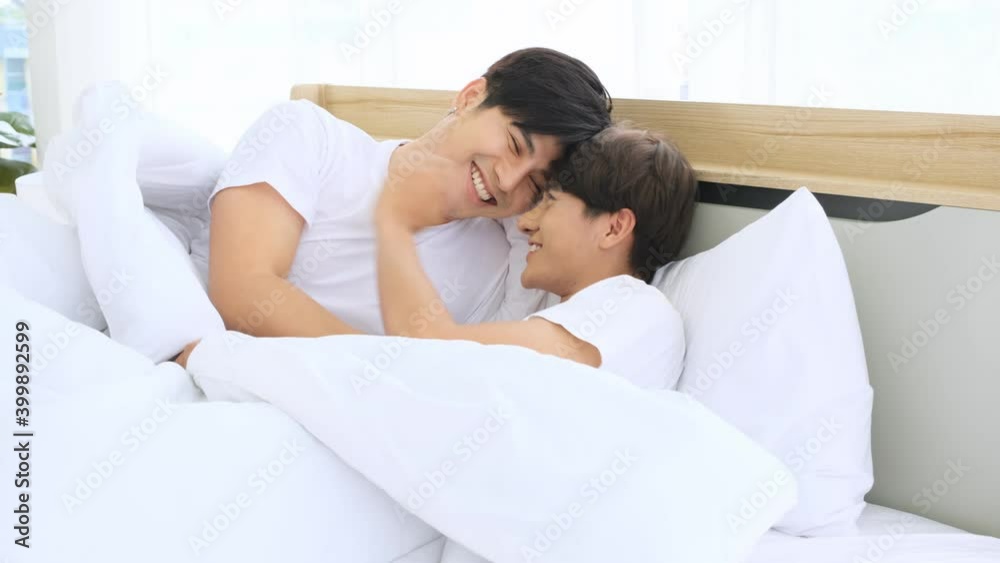 Two lgbt gay men play under and open the blanket to make fun of each other in their bedroom in the morning.