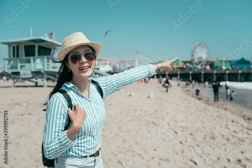 pretty young asian chinese woman standing and point finger at amusement park. cheerful beautiful girl traveler relax on beach relax on holidays. happy female standing by lifeguard stand on sunny day