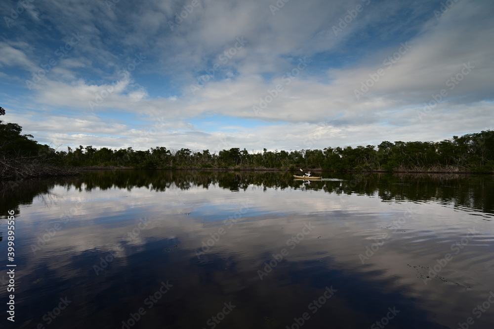 Distant kayaker in Coot Bay Pond, Everglades National Park, Florida under winter cloudscape reflected in tranquil water.