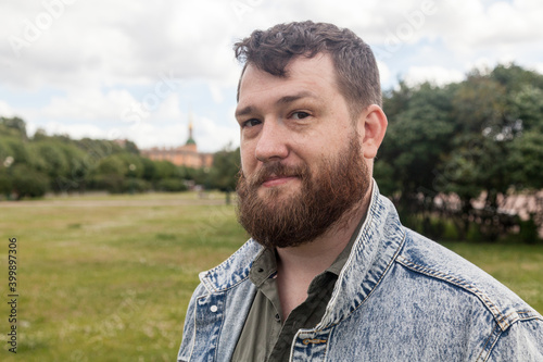 Bearded brown haired middle-aged man sitting in summer park