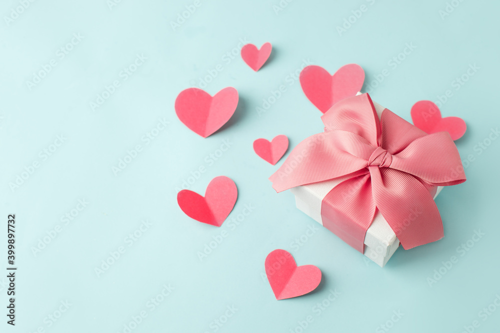 Stylish gift box with big pink bow and tender paper craft pink hearts on blue background, copy space, Greeting card, banner, flyer, postcard for Saint Valentine day, romance holiday, wedding, birthday