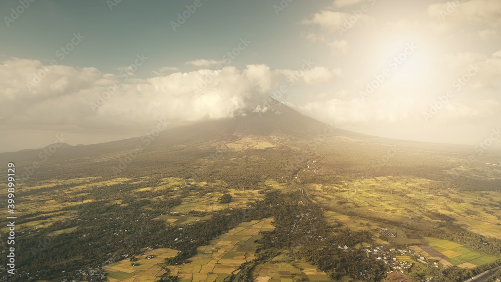Tropic sun farmlands at green volcano hillside valley aerial. Legazpi countryside at tropical Philippines. Tourist attraction of Mayon mount erupt. Clouds haze eruption over mountain peak at sunlight