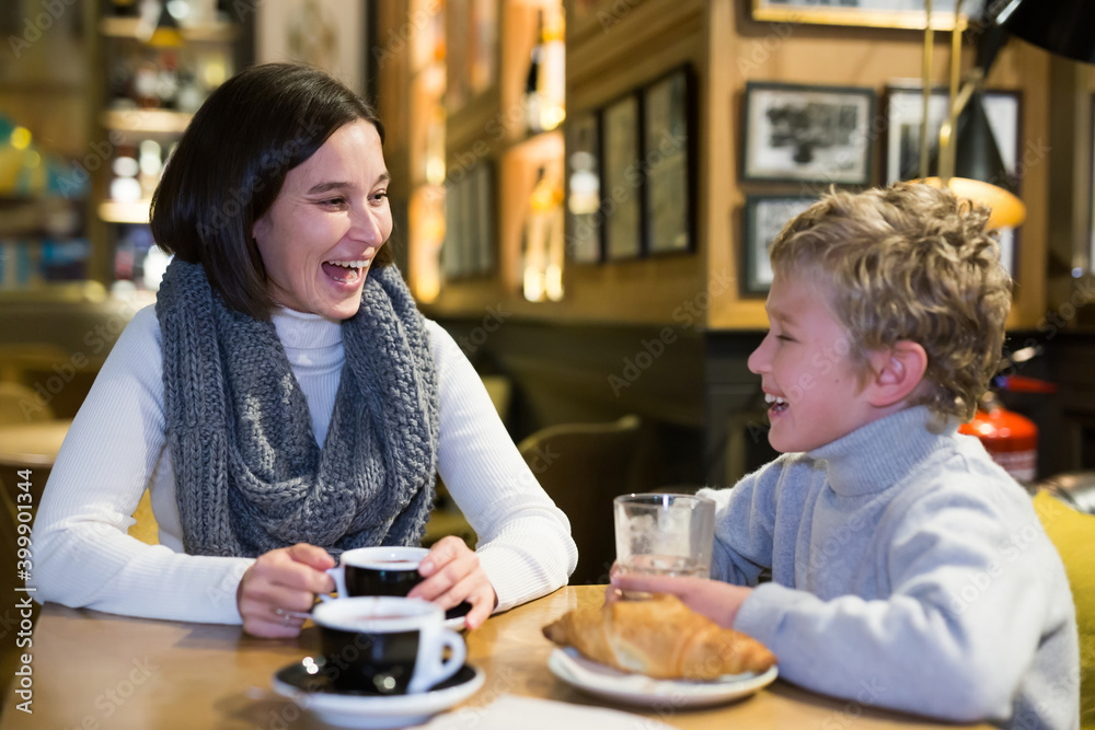 Young mother with tween son having fun at cafe, drinking coffee and cocoa with croissants and friendly talking