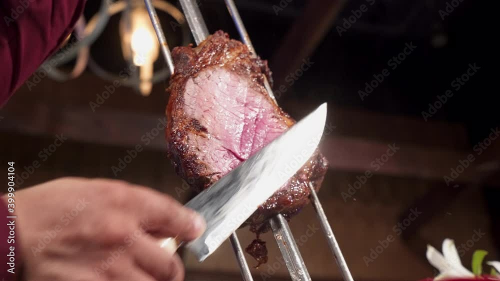 Gaucho slices juicy beef from skewer at Brazilian steakhouse, slow motion 4K