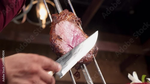 Gaucho slices juicy beef from skewer at Brazilian steakhouse, slow motion 4K