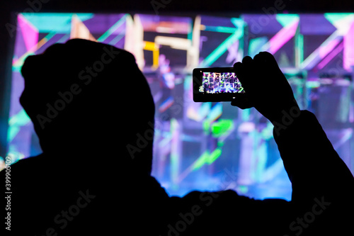 Silhouette of man with a phone photographing a light show