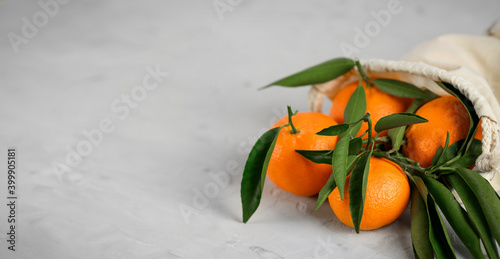 Fresh mandarin citrus fruits in flax burlap bag on grey cement background. Copy space.