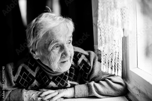 An old woman portrait sitting at her home. Black and white photo.