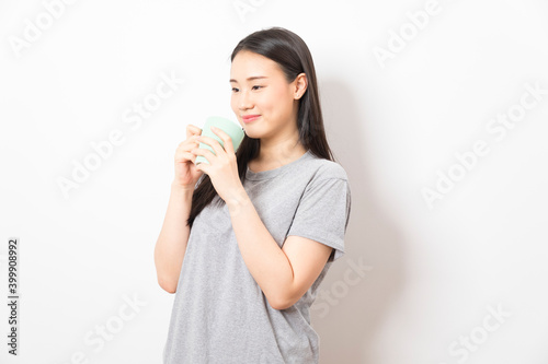 Gorgeous Asian woman drinking coffee and smiling standing over white background.