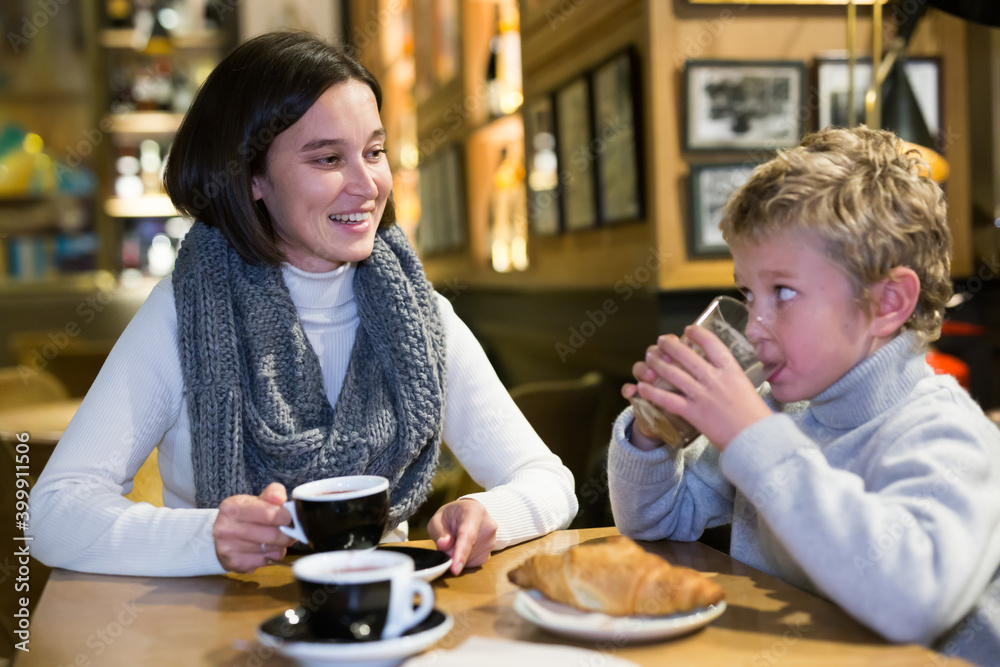 Cheerful woman spending time with her preteen son in cozy cafe. Happy family moments