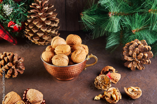 Walnuts in a tin cup, whole and chopped, next to the filling and shells. Presented in a New Year's composition with fir cones. Home storage of winter preparations