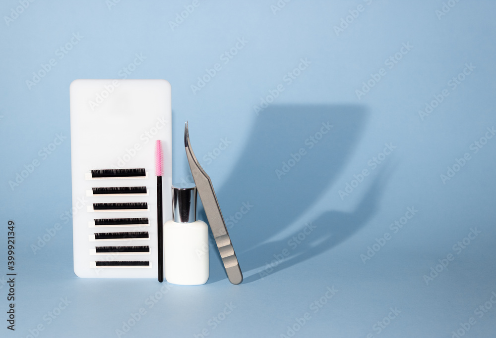 Tablet with artificial eyelashes, brush, glue and tweezers for eyelash extension. Tools for the lashmaker. Blue background, levitation. Free space for text. Tablet with artificial eyelashes, brush, glue and tweezers for eyelash extension. Tools for the lashmaker. Blue background, levitation. Free space for text.