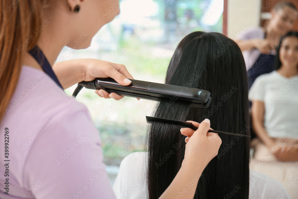 Female hairdresser straightening woman's hair in salon