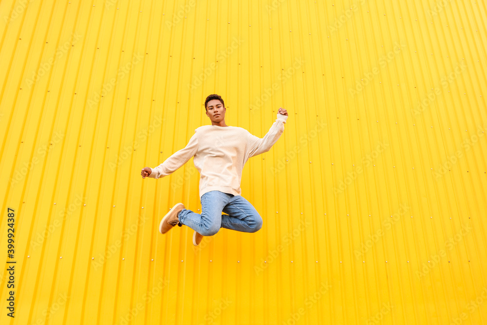 Stylish jumping young African-American man against color wall