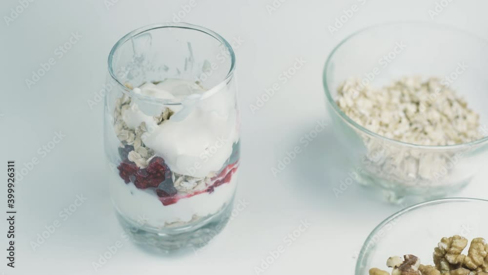 Female preparing gluten-free weight-loss-friendly snack. Cottage cheese, oatmeal, raspberry jam and walnuts. Preparing organic snack for achieving wellness and weight-loss goals