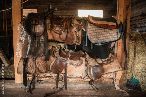 Leather saddles  soft blankets  steel stirrups and other riding equipment in the wooden stable on the ranch.