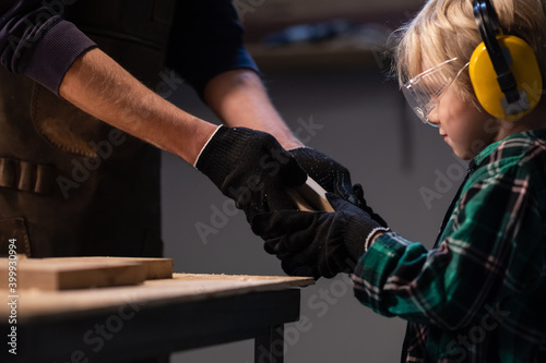 an experienced carpenter gives his little assistant carpentry tools in the workshop