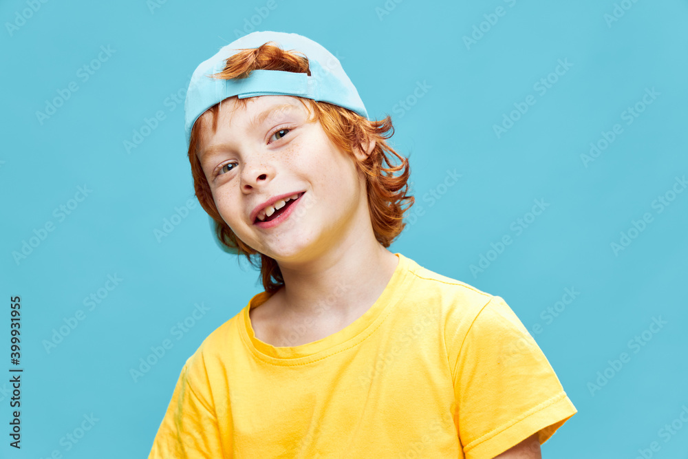 Cheerful red-haired boy in a yellow t-shirt with a blue cap on his head childhood smile Cheerful red-haired boy in a yellow t-shirt with a blue cap on his head childhood smile