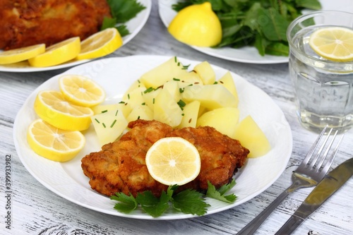 Wiener schnitzel and boiled potatoes.  Decorated with chopped chives, sliced lemon and parsley, white table.