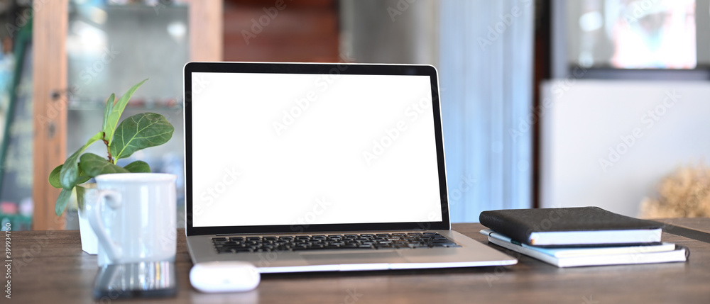 An open computer laptop, coffee cup, notebook and plant on wooden table. Blank screen monitor for graphic display montage. An open computer laptop, coffee cup, notebook and plant on wooden table. Blank screen monitor for graphic display montage.