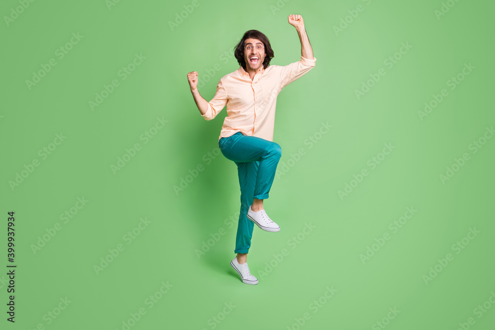 Full length body size view of nice cheerful guy jumping rejoicing having fun attainment isolated over bright green color background Full length body size view of nice cheerful guy jumping rejoicing having fun attainment isolated over bright green color background