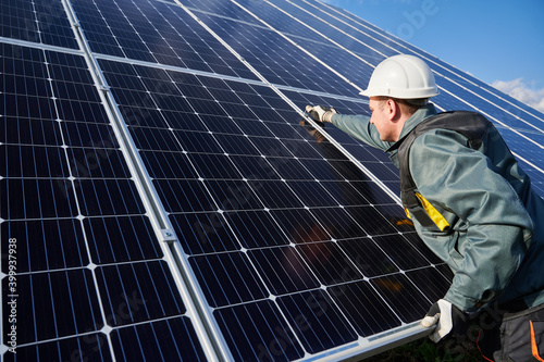 Man technician in safety helmet repairing photovoltaic solar module. Electrician in gloves maintaining solar photovoltaic panel system. Concept of alternative energy and power sustainable resources.