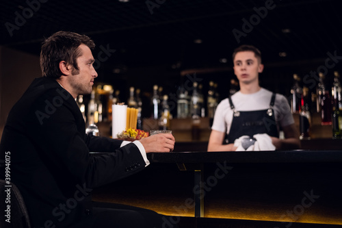 a young man drinks a cocktail at the bar, communicates with the bartender.