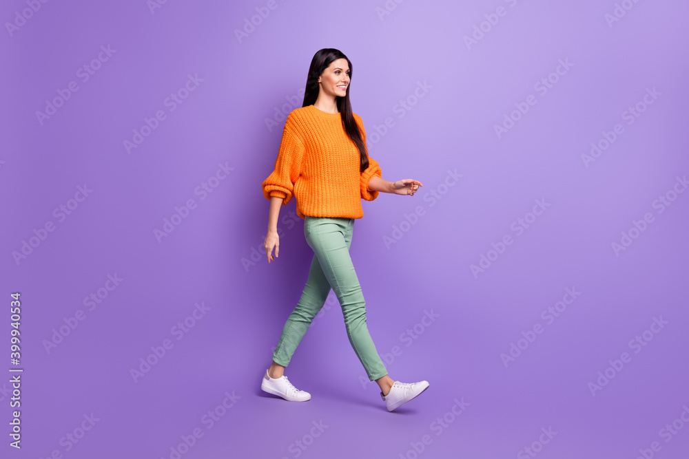 Full length body size photo of young girl walking forward in green pants sweater looking copyspace isolated on vivid purple color background