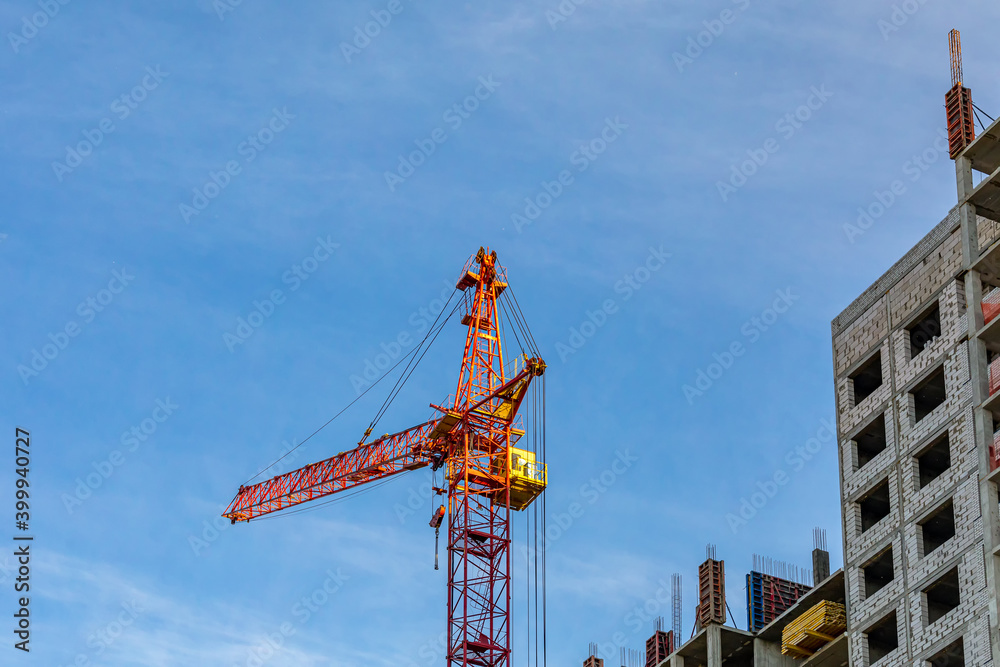 Red crane at a construction site against a blue sky. Construction of a typical multi-storey building.