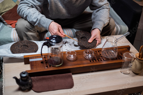 Close up. A tea seller breaks off a piece of strong black tea with a tea needle for sale in a tea shop