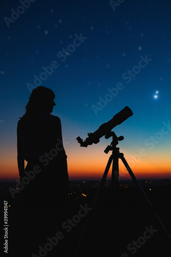 Woman looking at night sky with amateur astronomical telescope.