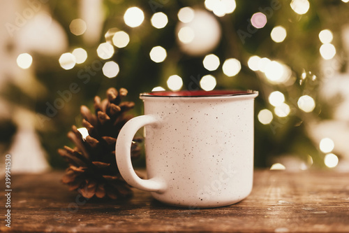 Cup of tea and pine cone on rustic wooden background at Christmas tree lights bokeh. Merry Christmas and Happy Holidays!