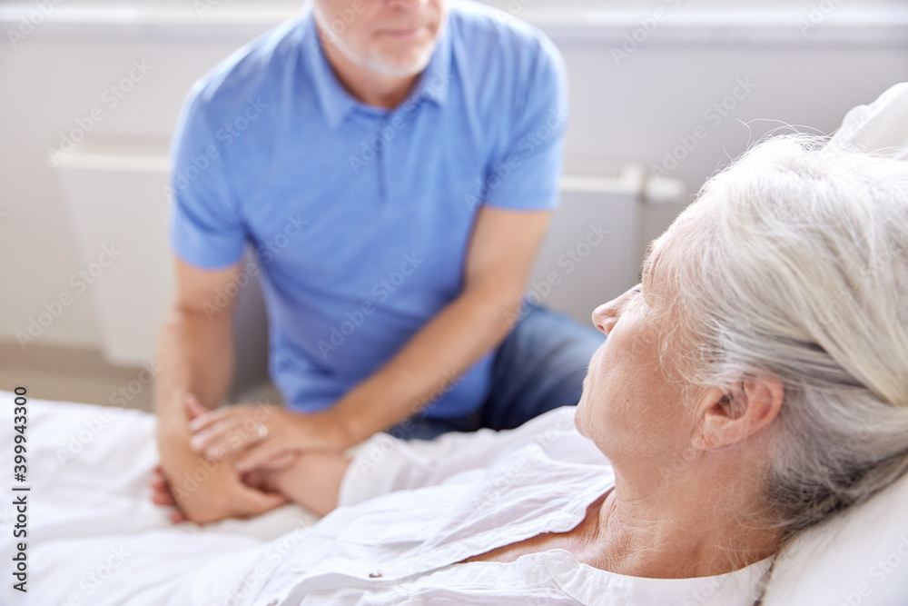 medicine, healthcare and people concept - senior man visiting and cheering his woman lying in bed at hospital ward medicine, healthcare and people concept - senior man visiting and cheering his woman lying in bed at hospital ward