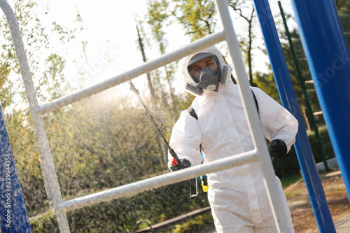 Man in hazmat suit spraying disinfectant on outdoor gym's equipment. Surface treatment during coronavirus pandemic © New Africa
